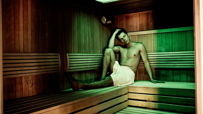 Uomo che si rilassa in una sauna di legno con asciugamano sotto luce verde soffusa